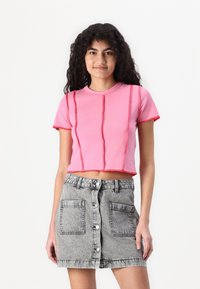 Ροζ κοντομάνικο μπλουζάκι με κοντά μανίκια και αντιθέτονται κόκκινες ραφές. Συνδυάζεται με γκρίζα τζιν φούστα με μπροστινά κουμπιά και μεγάλες τσέπες.