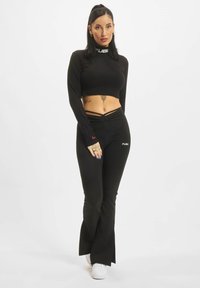 Čierny crop top s vysokým výstrihom a logom, skombinovaný s priliehavými čiernymi nohavicami s rozšírenými nohavicami a bočným detailom loga.