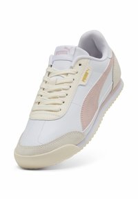 Baskets en cuir blanc avec des accents rose clair et une semelle en caoutchouc beige. Elles présentent un design à lacets et un logo Puma classique sur le côté et sur la languette.