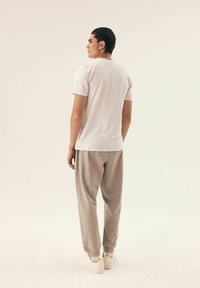 Biała koszulka z krótkim rękawem połączona z jasnoszarymi spodniami dresowymi z elastycznymi mankietami. Model ma na sobie białe sneakersy i stoi na neutralnym tle.