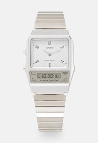 Montre Casio argentée avec un cadran analogique rectangulaire blanc, des index horaires noirs et un affichage numérique. Bracelet en métal avec finition brossée. Résistante à l'eau.