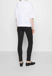 Valkoinen ylisuuri lyhythihainen paita, jossa suora helma, yhdistetty mustiin kapealahkeisiin housuihin; minimalistinen muotoilu, sileä pinta ja hienovarainen takana oleva logodetalji.