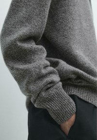 Szary dzianinowy sweter o długich rękawach, z prążkowanymi ściągaczami i luźnym krojem, zestawiony z czarnymi spodniami.