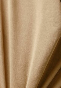 Mjukt beige tyg med en slät textur, med subtila veck och en matt yta, vilket indikerar ett lätt och ventilerande material.