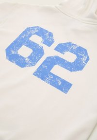 Hoodie bianco con una grande grafica "62" blu, usurata, stampata sul davanti. Tessuto morbido con una vestibilità rilassata e polsini a coste.