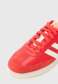Rød sneaker med en kombination af glat læder og ruskind, med hvide striber og matchende snøringer samt en struktureret gummisål.