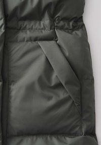 Dunkelgrüne gepolsterte Jacke mit einer sichtbareren Seitentasche, glatter Textur, genähten Details und einem weichen, glänzenden Finish.