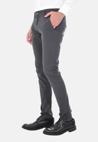 Pantaloni grigi a fantasia con vestibilità slim, dotati di tasche laterali e chiusura con bottone. Indossati con scarpe eleganti nere, evidenziando il design sartoriale.