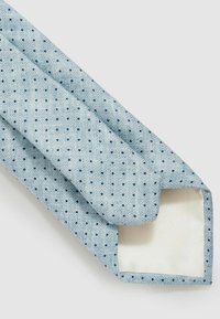 Corbata azul claro con una superficie texturizada, que presenta un patrón de pequeños puntos azul oscuro, y un forro interior suave de color crema.