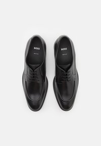 Scarpe in pelle nera con finitura liscia, punta tonda e design con lacci. Presentano una suola testurizzata e un marchio all'interno.