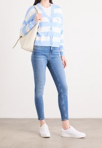 Cardigan de rayas azul claro y blanco con escote en V y botones, combinado con jeans ajustados azules y zapatillas blancas. Incluye un bolso de hombro crema.