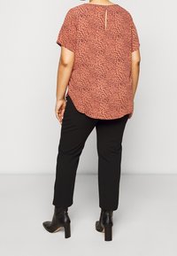 Lehký volnější top s krátkým rukávem v barvě rezavého plechu s černým abstraktním potiskem; kombinujte s upravenými černými kalhotami a kotníkovými botami.