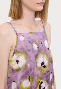 Camisole floral violet avec bretelles spaghetti, affichant une texture soyeuse et un mélange de grands motifs floraux blancs et verts.