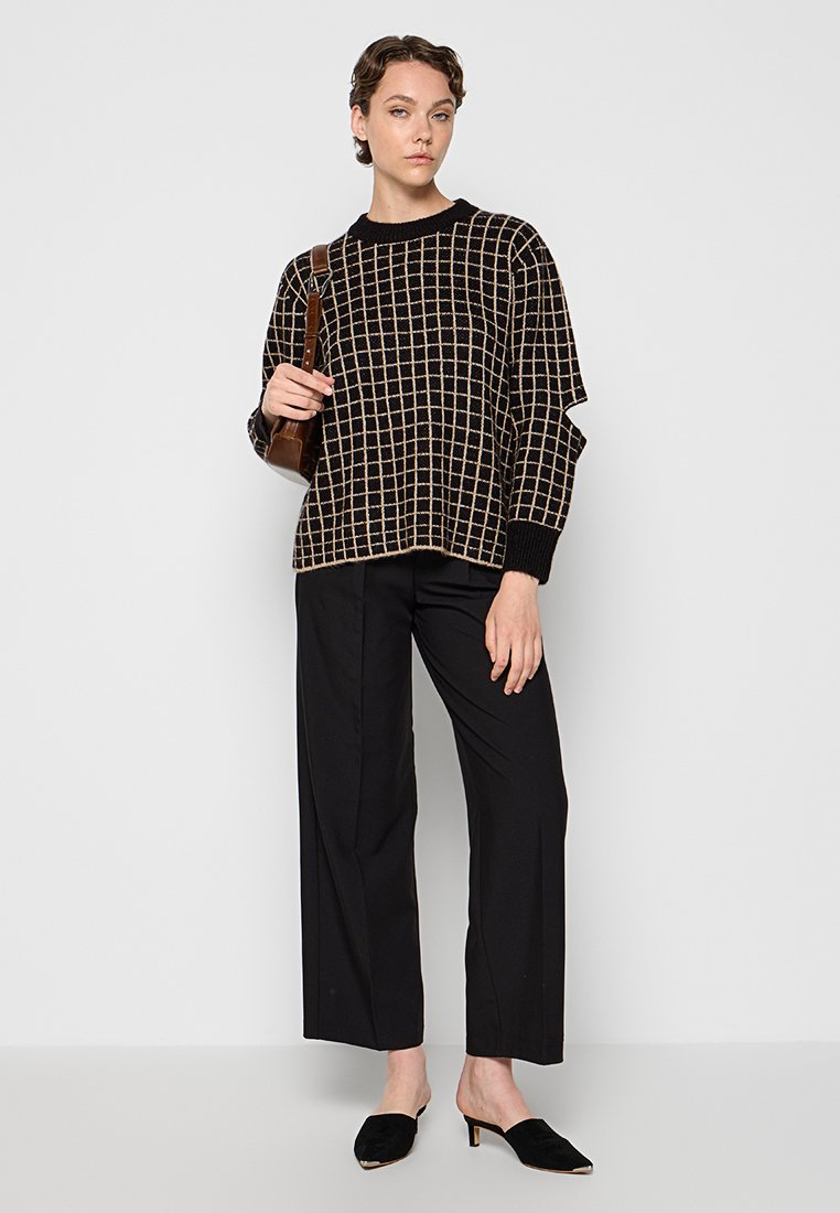 Schwarzer und cremiger Pulli mit übergroßem Gittermuster, kombiniert mit schwarzen weit geschnittenen Hosen und schwarzen Mules; weiche Textur und lässige Passform.