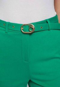 Groene broek met een gladde textuur, voorzien van een gouden ovale gesp riem en gouden eyelets, ontworpen met zijzakken en een getailleerde pasvorm.