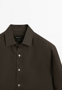 Dark brown linen button-up shirt with collar and white buttons, shown from chest to shoulder on a white background.