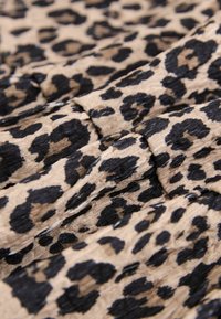 Likteņa raksta audums ar melniem un brūniem plankumiem uz bēša fona; viegls, krokains tekstūra, salocīts kā slāņi.