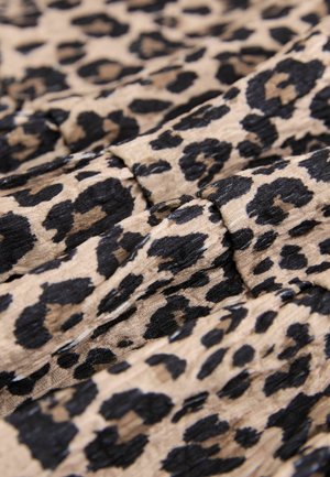 Likteņa raksta audums ar melniem un brūniem plankumiem uz bēša fona; viegls, krokains tekstūra, salocīts kā slāņi.