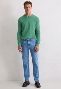 Grüner, gestrickter Pullover mit langen Ärmeln, kombiniert mit hellblauen Jeans. Schwarze klobige Schuhe vervollständigen das Outfit. Minimalistisches Design, legere Passform.