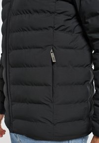 Giacca a vento nera con texture trapuntata, zip laterale e vestibilità slim. Il tessuto appare opaco e leggero, adatto per il freddo.