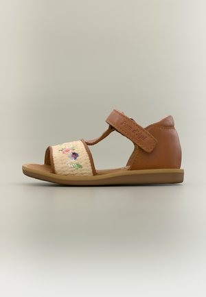 Ruskea taaperoiden sandaali, jossa on kukkakirjailtu vaniljanvärinen kangas edessä ja säädettävä nilkkaremmi Tarrakiinnityksellä.