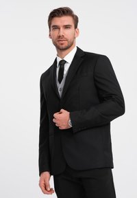 Musta puku, jossa on istuva takki ja housut, valkoinen paita, musta solmu ja harmaa liivi. Huomattavat yksityiskohdat sisältävät tyylikkäät kaulukset ja kellon.