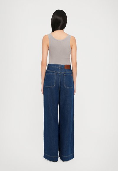 Gray ribbed tank top with blue wide-leg jeans featuring a leather patch, side pockets, and a slightly frayed hem.