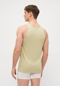 Débardeur côtelé vert olive avec de larges bretelles, un col rond et des fentes sur les côtés, porté sur des boxer blancs.