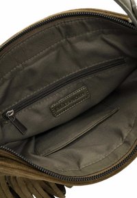 Brown suede handbag interior with a smooth olive green lining, featuring a zippered pocket and a brand label embossed on a leather patch.