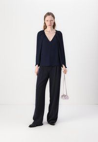 Top blu navy con scollo a V e maniche drappeggiate, abbinato a pantaloni larghi blu navy e una borsa lilla chiara. Tessuto morbido e vestibilità su misura.