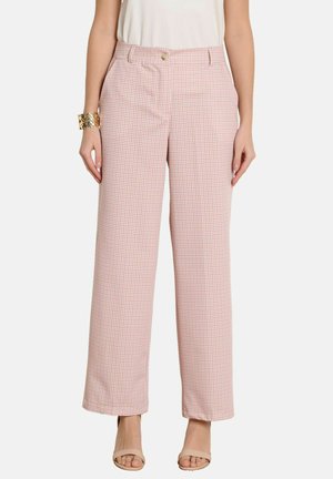 Žena nosi ružové a bielo kockované nohavice s vysokým pásom a širokými nohavicami s prednými vreckami a béžový tielkový top, doplnené béžovými sandálmi.