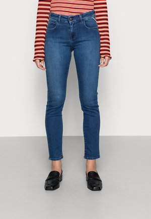 Jeans de tiro alto y ajustados en denim azul oscuro, con bolsillos frontales y un efecto de desvanecimiento ligero. Combinados con mocasines negros.