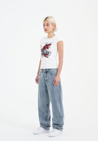 White t-shirt with red fish graphic, short sleeves. Paired with loose-fitting light blue jeans and white sneakers. Simple, casual design.