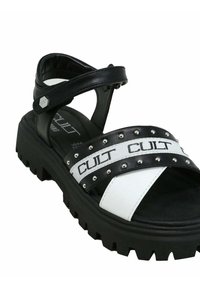 Sandali in bianco e nero con suole spesse, dotati di cinturini con borchie e un audace marchio "CULT". Realizzati in materiale sintetico con una superficie liscia.