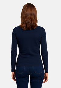 Maglietta a maniche lunghe di colore blu navy realizzata in tessuto morbido, con un design aderente, scollatura rotonda e texture liscia senza motivi né decorazioni.