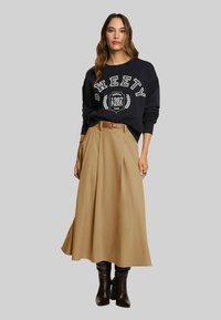 Sweat-shirt bleu marine avec texte et motif blanc, associé à une jupe plissée beige et des bottes marron montant aux genoux, ceinturé à la taille.