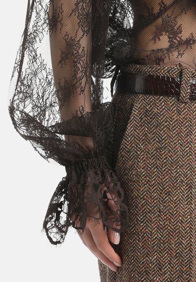 Bruine kanten top met uitlopende mouwen en ingewikkelde bloemmotieven, gecombineerd met houndstooth tweed broeken in aardetinten en een glanzende riem.