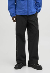 Jachetă ușoară albastră cu manșete elastice și fermoar în față, purtată cu pantaloni negri și încălțăminte neagră cu o talpă texturată.