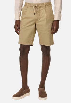 Shorts caqui con cintura ajustable, pliegues frontales y bolsillos laterales. Combinados con unos zapatos de ante marrón de tipo slip-on. Detalle de dobladillo plano.