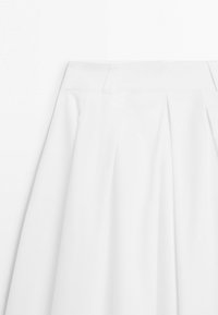 Hvid plisseret nederdel med bred linning og bæltestropper, vist mod en ensartet hvid baggrund.