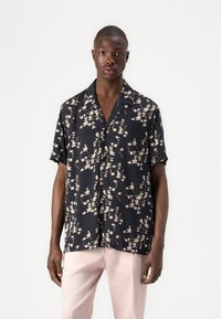 Short-sleeve shirt in dark navy fabric with a floral pattern in beige tones; features a collar and button-down front. Paired with light pink pants.