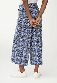 Pantalons larges à motifs bleus avec un design floral noir et des accents blancs, fabriqués en tissu léger. Dispose d'une taille élastique.