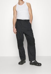 Czarne spodnie z kontrastowymi �łatami na kolanach, teksturowaną powierzchnią i paskiem w talii. Noszone z białym topem na ramiączkach i czarnymi klapami.