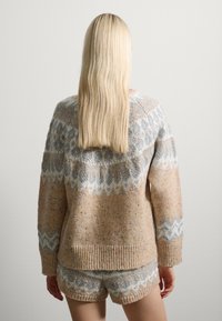 Strickpullover und passende Shorts in pastellbeige mit grauen Mustern. Der Pullover hat gerippte Bündchen und einen Saum sowie eine weiche, strukturierte Oberfläche.