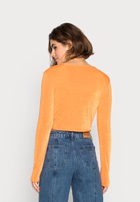 Camisola laranja de manga longa com uma textura suave e um corte confortável, combinada com jeans azuis de cintura alta com bolsos traseiros.
