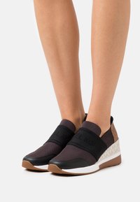 Chaussures de sport noires et grises avec une semelle compensée. Dotées de sangles élastiques, d'un talon à motif et d'une tige texturée. Semelle extérieure en caoutchouc.