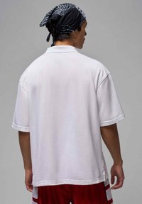 Biała, oversize'owa koszulka polo z krótkimi rękawami, teksturowana tkanina, luźny krój, zestawiona z czerwonymi szortami z białymi paskami.