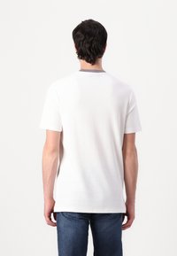 White short-sleeve t-shirt with a round neckline and a smooth texture, paired with blue jeans. Simple design, no prominent patterns or accents.