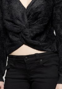 Czarny, puszysty, krótki sweter z ozdobnym skręceniem z przodu, zestawiony z czarnymi, dopasowanymi dżinsami z guzikiem i bocznymi kieszeniami.