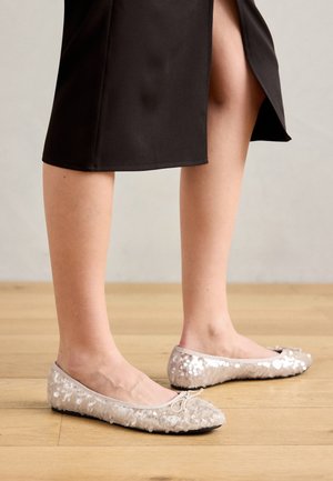 Flat ballet shoes in light beige, covered in shiny sequins. Features a soft, rounded toe and a decorative bow at the front.